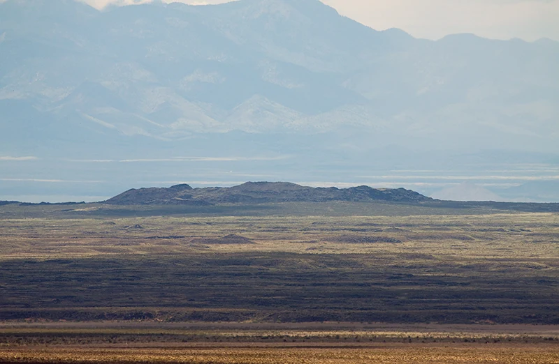 Low dark rim of Jornada del Muerto Volcano across a sunlit New Mexico plain, with mountains beyond