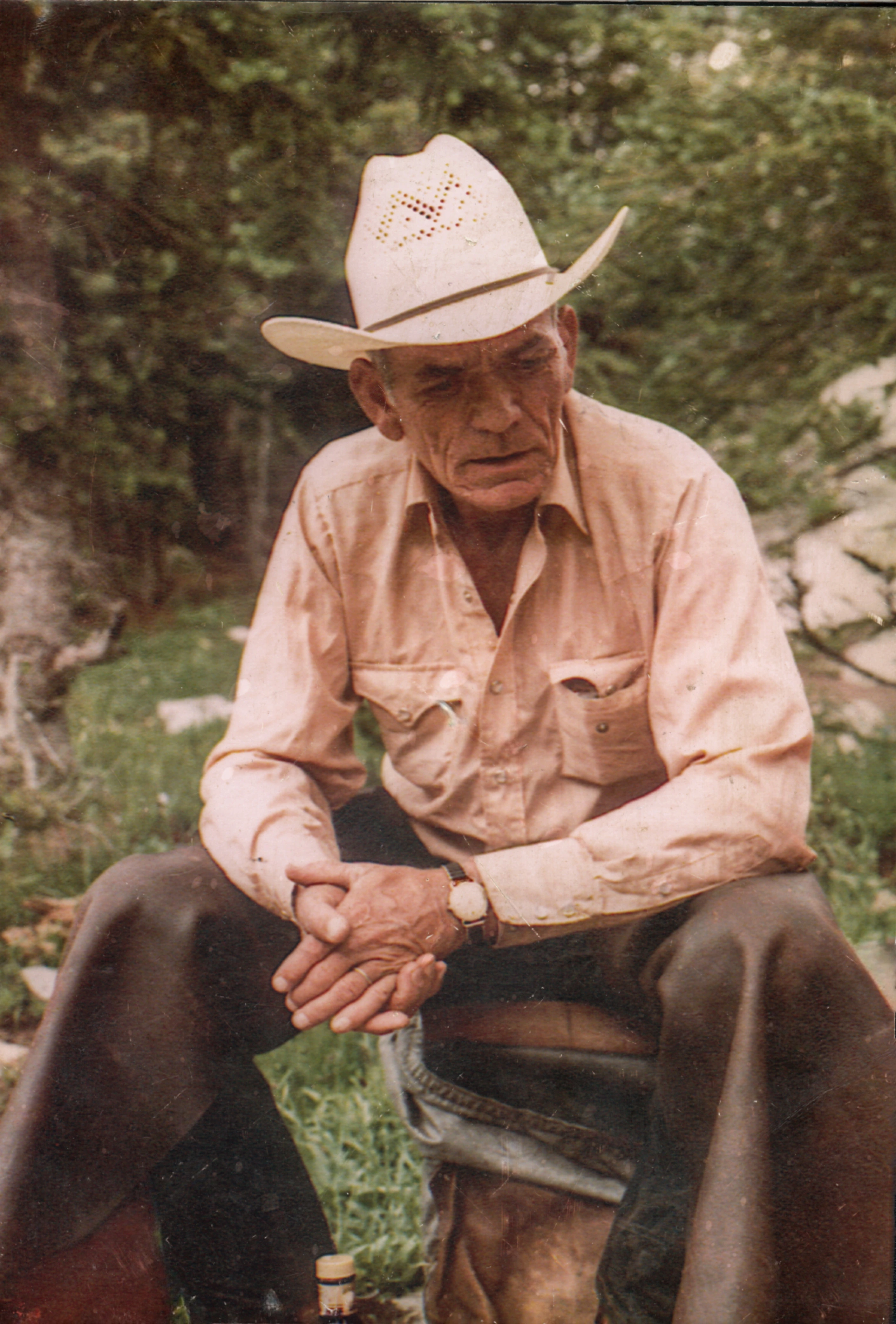 Bob Goode seated outdoors in a cowboy hat, with his hands clasped.