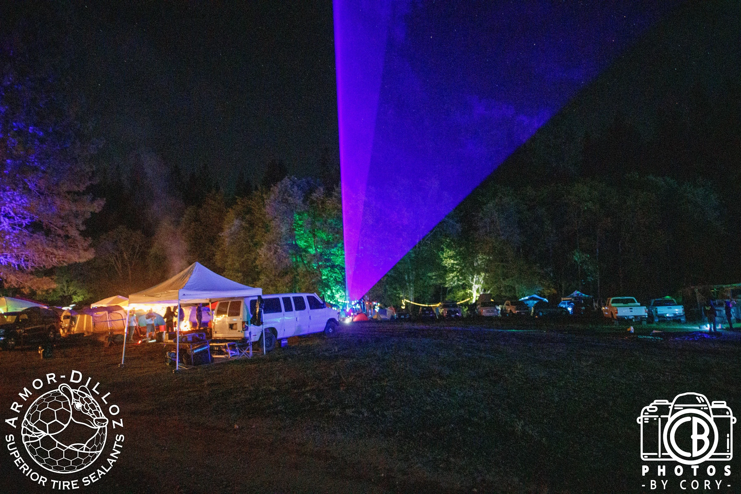 Purple laser beams fan out above the festival camp at night.