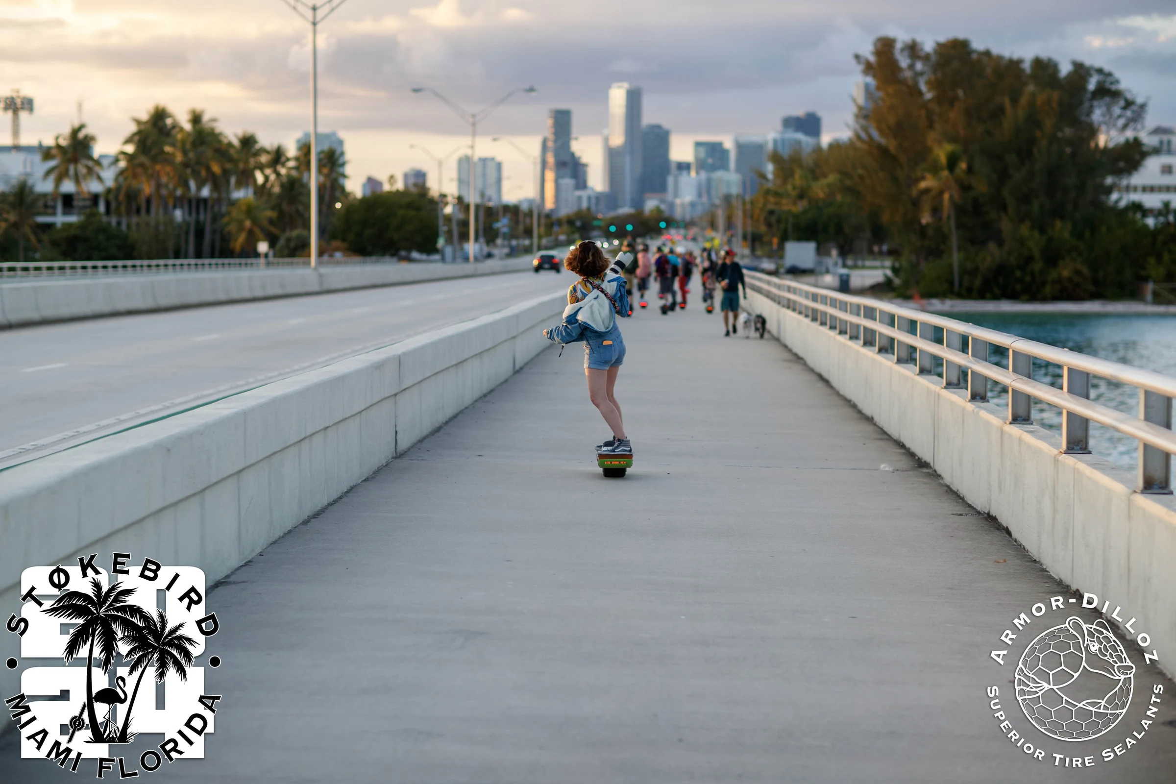 Onewheel riders crossing a bridge toward the Miami skyline in the evening light.